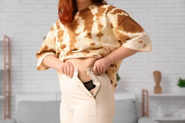 Image of woman trying to do her trousers up after pregnancy weight gain Bromyard